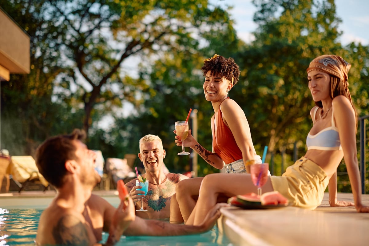 Multiracial group of carefree friends talking and drinking cocktails while enjoying summer at the pool