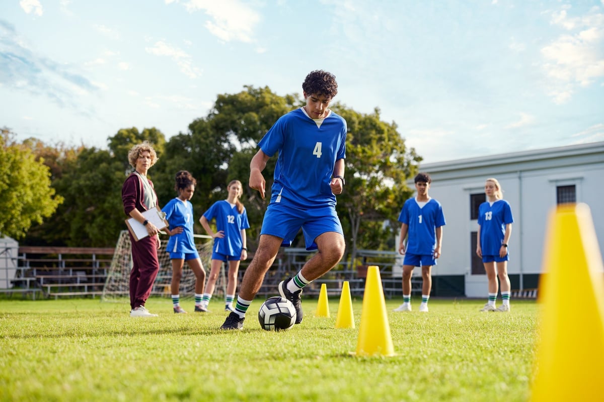 Teenager dribbling soccer ball through cones during training