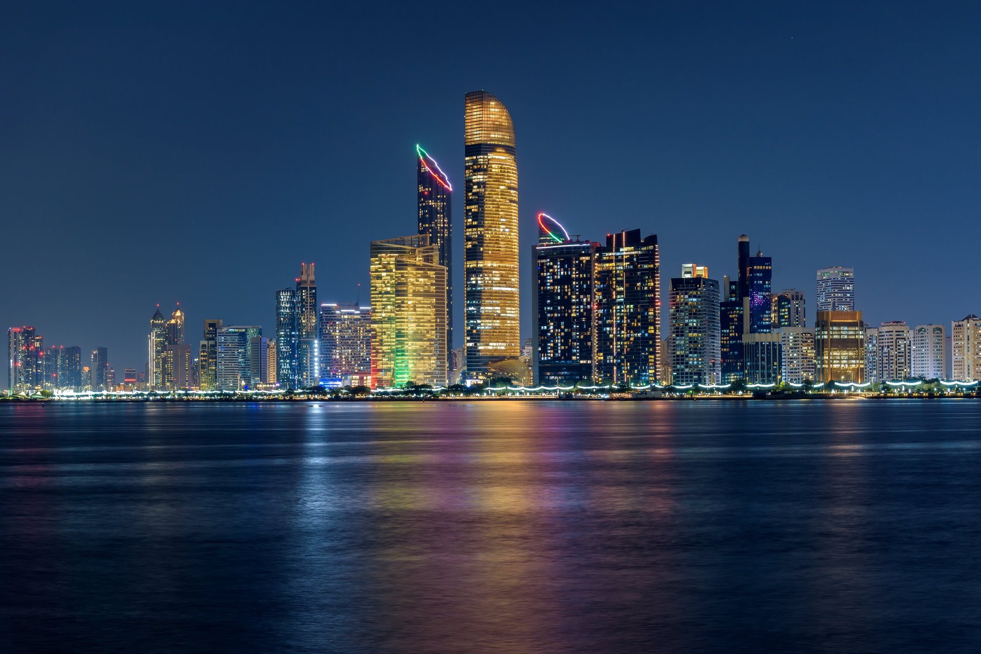 Vibrant night view of the illuminated Abu Dhabi waterfront with modern skyscrapers reflecting across the calm gulf waters