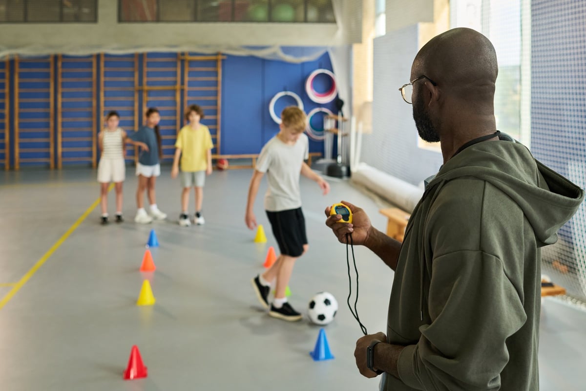 Coach timing kids dribbling soccer ball through cones during training