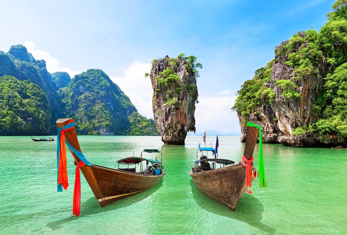 Traditional Thai longtail boat on turquoise water among limestone karsts in Phang Nga Bay, Thailand.
