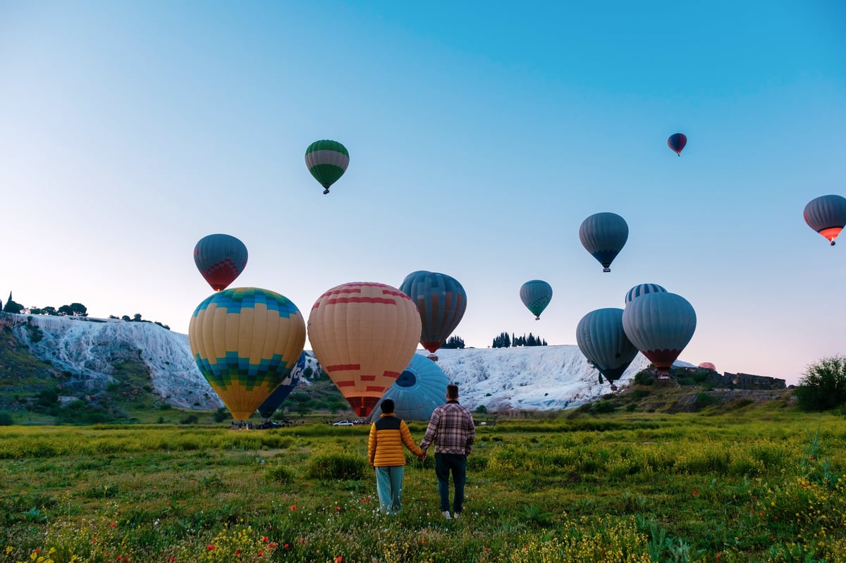 Colourful hot air balloons soaring above the white terraces of Pamukkale in Türkiye.