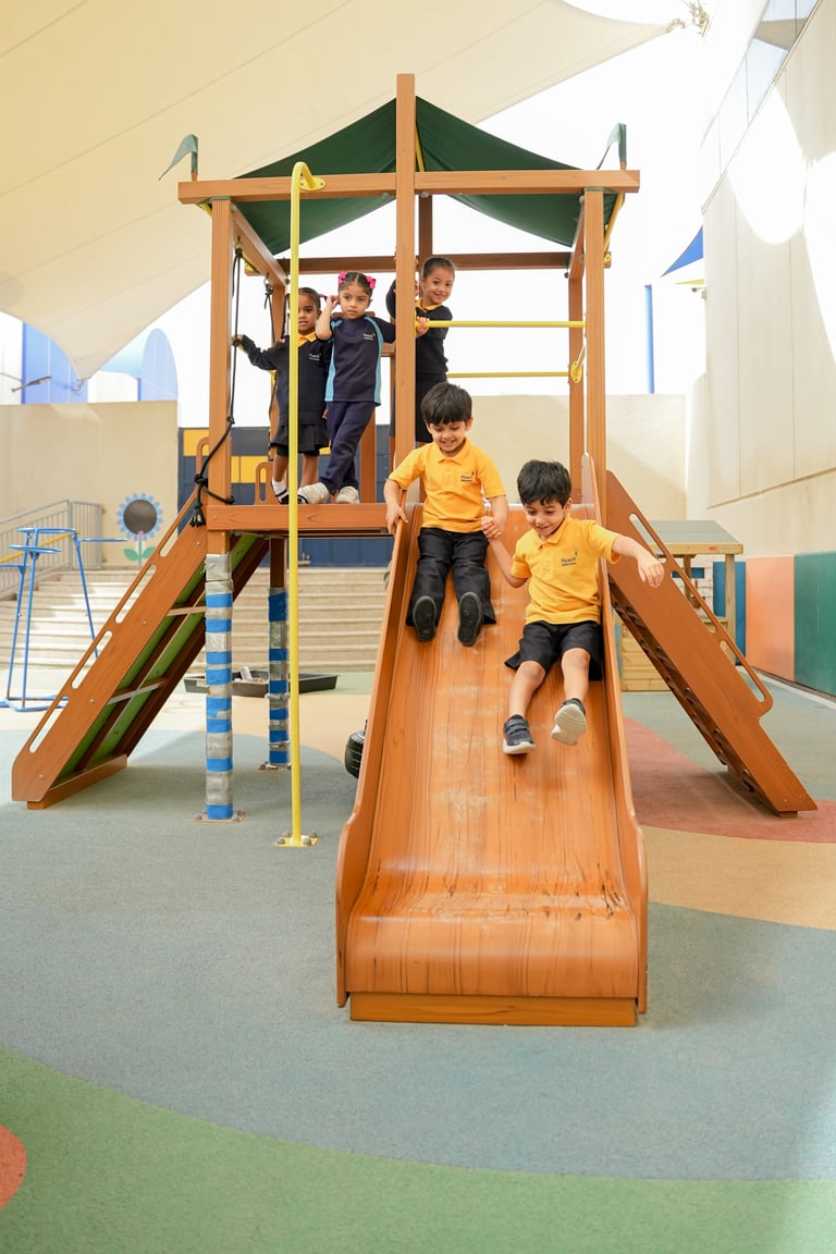 Children playing on a wooden playground structure with a slide and climbing features in an indoor gym setting