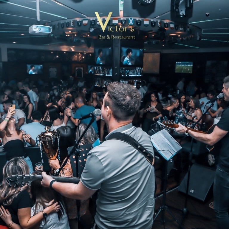 Crowded nightclub dance floor at Victors Bar & Restaurant with DJ booth, blue lighting, and people dancing