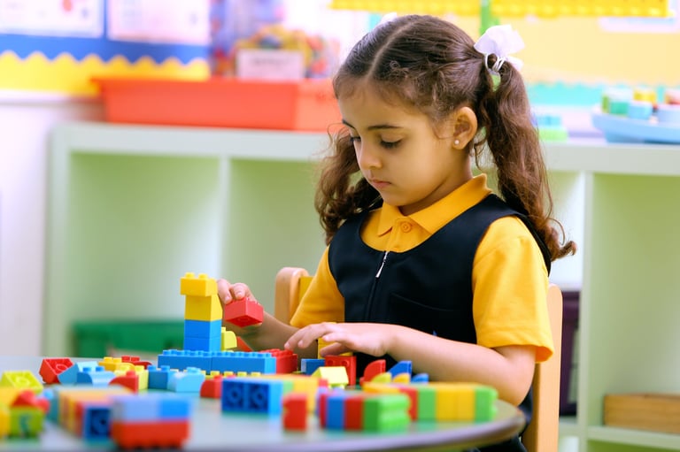 Young girl in yellow and black uniform playing with colorful building blocks at a table in a classroom