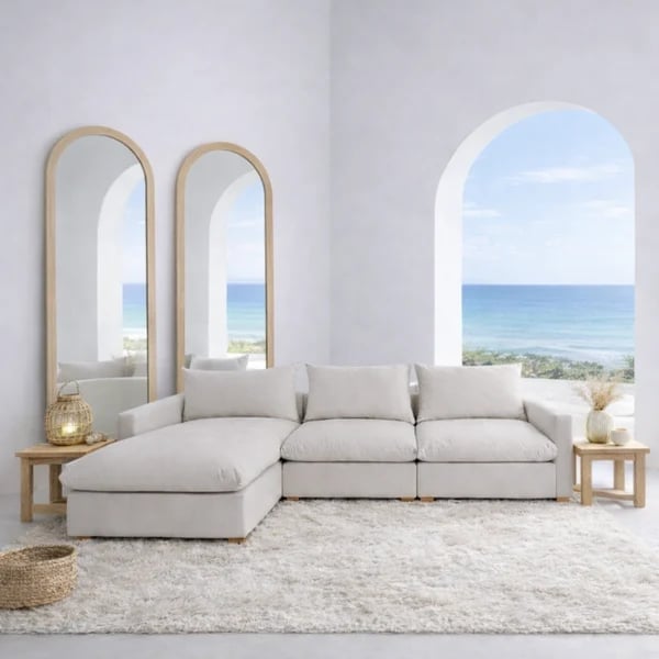 Modern light-filled living room with beige modular sofa, arched mirrors, and ocean view through large window