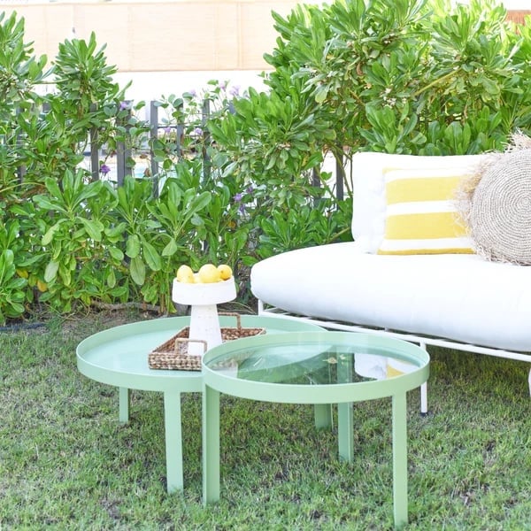 Outdoor patio seating area with mint green curved coffee table, white lounge chair with yellow and white striped pillows, and potted plants in background