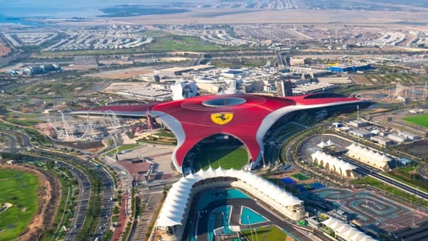Aerial view of Ferrari World Abu Dhabis iconic red building with prancing horse logo overlooking theme park and surrounding desert cityscape