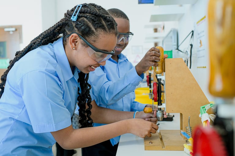 Two students in blue uniforms working on a wood construction project at a workbench in a classroom