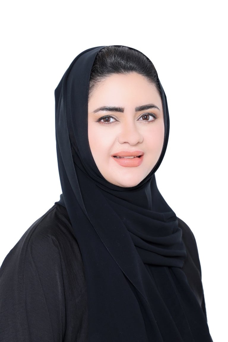 Portrait of a woman wearing a black hijab against a white background, facing the camera with a slight smile.