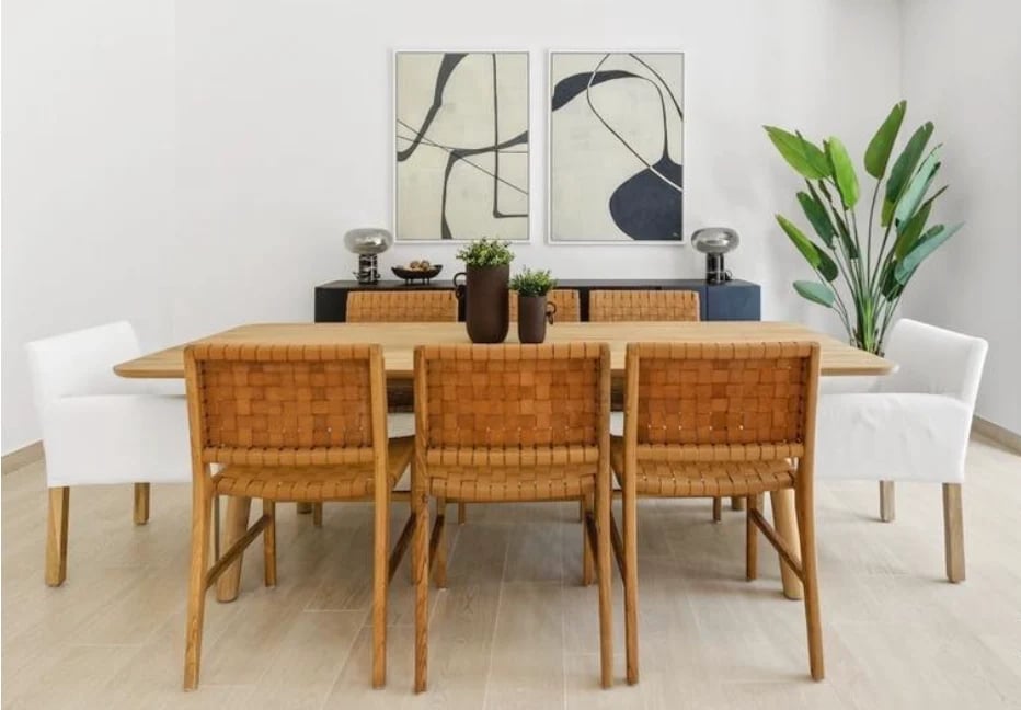 Modern dining room with wooden table, woven tan chairs, white accent chairs, minimalist wall art, and potted plant decor