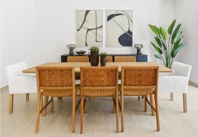 Modern dining room with wooden table, woven tan chairs, white accent chairs, minimalist wall art, and potted plant decor