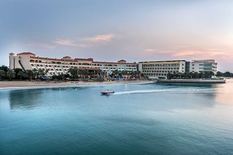 Beachfront resort buildings along a turquoise tropical bay with a small boat at dusk