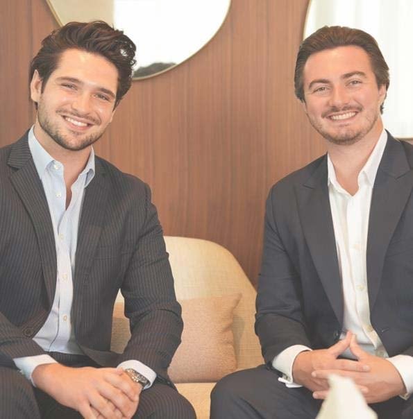 Two men in business suits smiling at the camera in an office setting with wood paneling and modern lighting