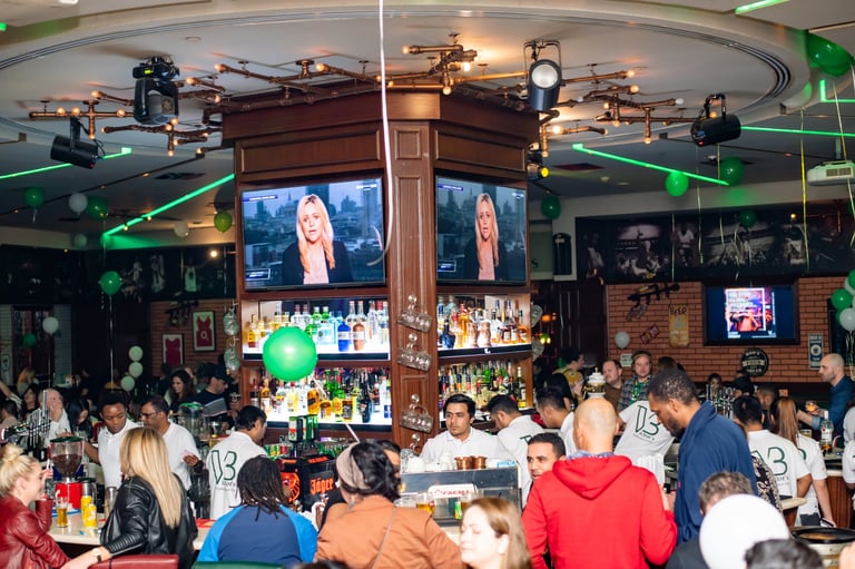 Crowded sports bar interior with large screens, illuminated bar counter, and patrons watching an event
