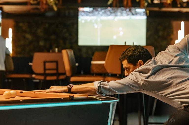 Man leaning over a pool table in a dimly lit bar with a projection screen visible in the background