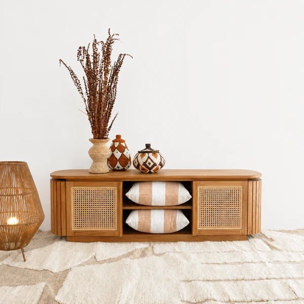 Wooden sideboard with rattan details, decorative dried grass arrangement, striped pillows, and woven pendant light on light background