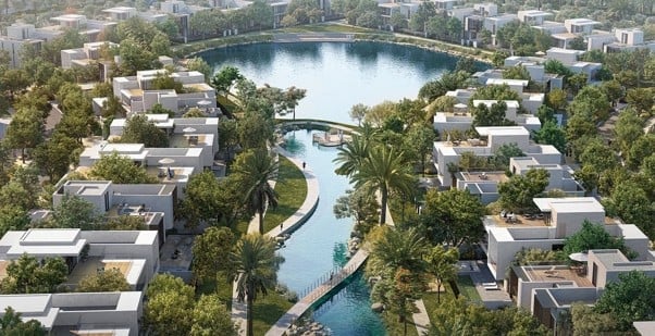 Aerial view of a planned residential community with modern white buildings surrounding a central blue lagoon and waterway with a bridge