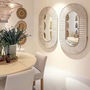 Modern dining room with two oval rattan mirrors, white round table, upholstered chair, and greenery in a vase