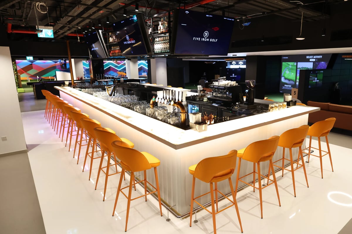 Modern bar with glowing white countertop and yellow bar stools in an upscale venue with screens and ambient lighting