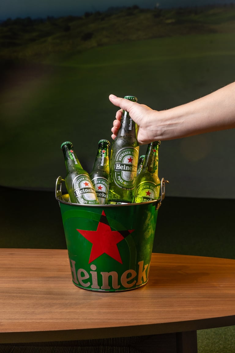 Hand reaching for a Heineken bottle from a green ice bucket filled with beer bottles on a wooden table