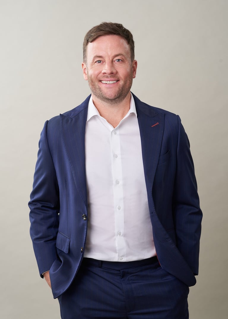 Professional portrait of a man in navy blazer and white shirt smiling at camera against neutral background