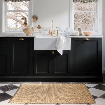 Modern bathroom with black cabinetry, white marble countertop, farmhouse sink, and natural fiber rug against geometric tile floor