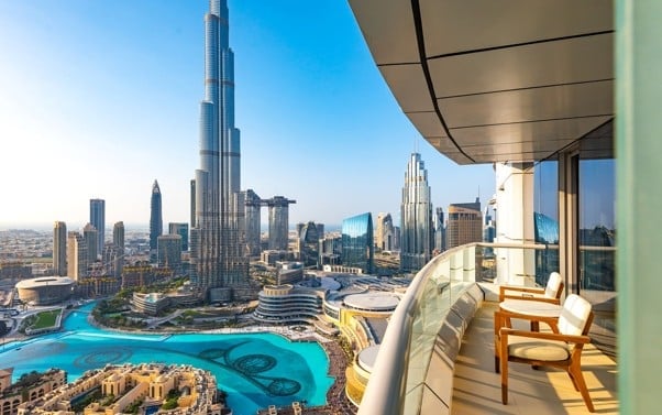 View from a luxury high-rise balcony overlooking Dubais skyline with Burj Khalifa, turquoise fountain, and modern buildings