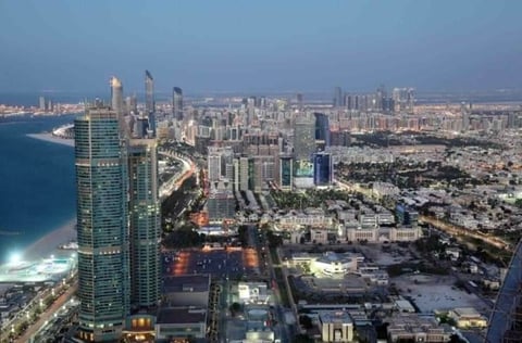 Aerial view of a sprawling coastal city at dusk with illuminated high-rise buildings and shoreline