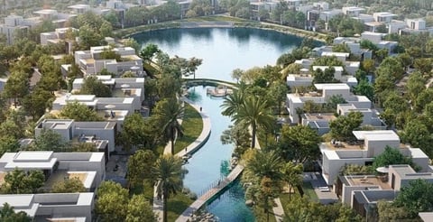 Aerial view of a planned waterfront community with modern white buildings, canals, palm trees, and a central blue lake with bridge