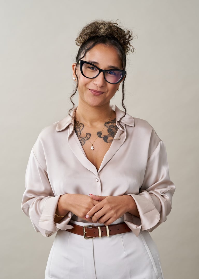 Woman wearing glasses and pink button-up shirt with brown belt, smiling at camera against neutral background