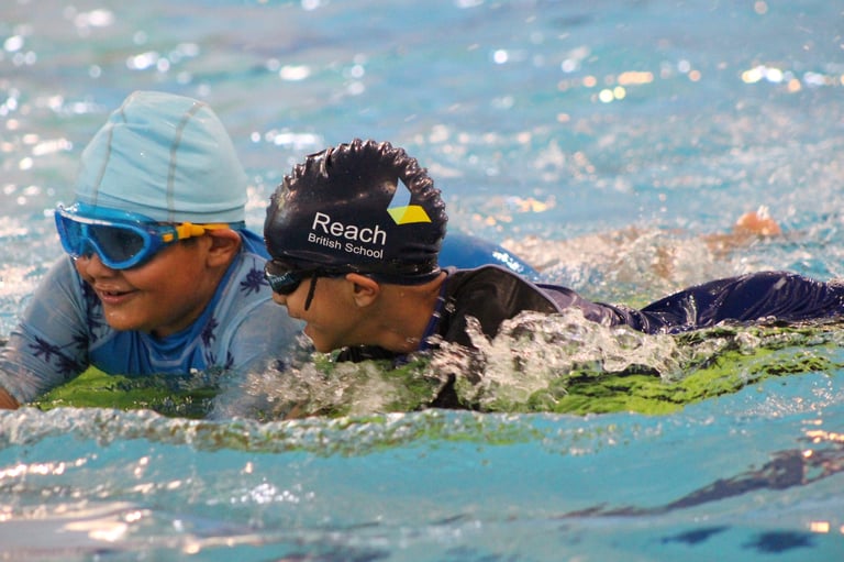 Two young swimmers in a pool wearing swim caps and goggles, practicing butterfly stroke during swimming lesson