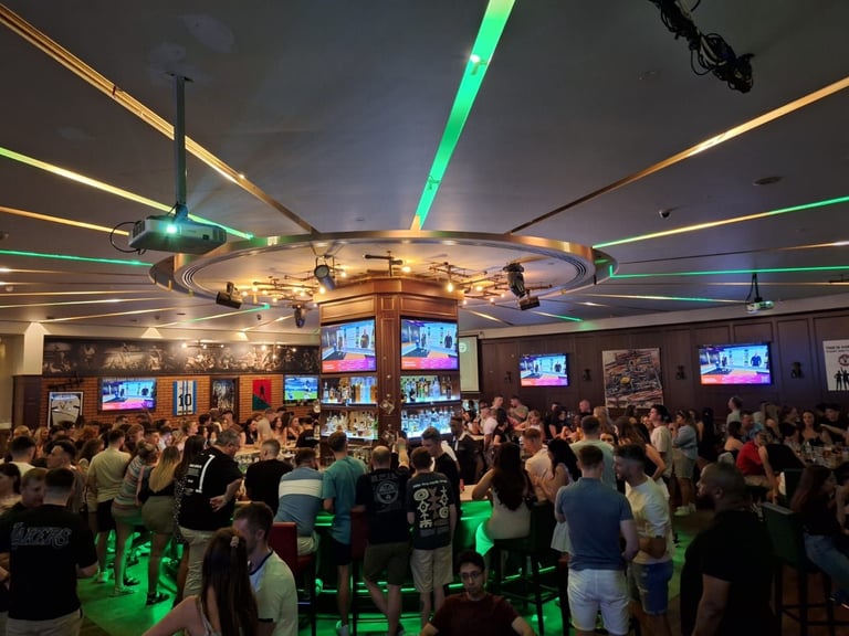 Crowded indoor venue with neon green lighting, multiple screens on walls, and illuminated ceiling fixtures