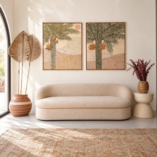 Modern minimalist living room with cream-colored curved sofa, botanical wall art, woven decor, and natural lighting from large windows